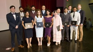 A group of 13 people stands on stage, dressed in formal attire, holding certificates.