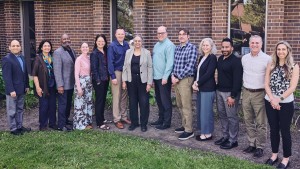 The thirteen members of the Dean's Cabinet pose outside in front of a brick building.