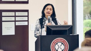 A woman stands at a podium, speaking into a microphone.