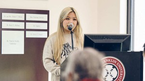 A young woman stands at a podium and speaks into a microphone.