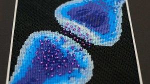 A cross-stitched depiction of a synapses, made with blue thread and beads.