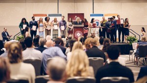 A large group of students are lined up on a stage, holding award certificates.