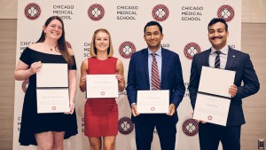 Four smiling students hold award certificates, standing in front of a white backdrop with the Rosalind Franklin University logo on it.