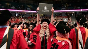 A woman in a graduation gown proudly holds up her diploma during the commencement ceremony.