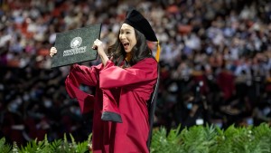 A woman in a graduation gown proudly holds up her diploma during the commencement ceremony.