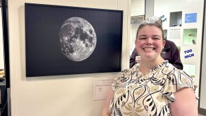 A smiling young woman stands next to a print of a high-resolution photo of the moon