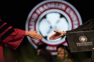 Two people extend their hands for a handshake during a graduation ceremony. A podium with the Rosalind Franklin University logo is visible.
