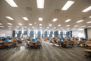 A spacious, well-lit area with rows of beige chairs and desks, each equipped with a desktop computer.