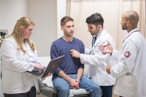 A medical team examines a seated man in a clinic. 