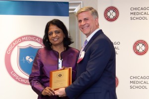 A woman and man stand smiling, holding a plaque at an event. The backdrop features the Chicago Medical School logo.