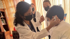 A young woman wearing scrubs and a white coat examines a boy as he sits on an exam table