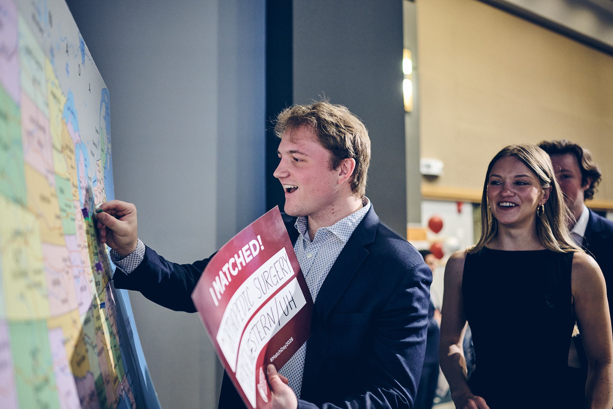 A man in a button-up shirt and suit jacket places a pin on a map of the United States